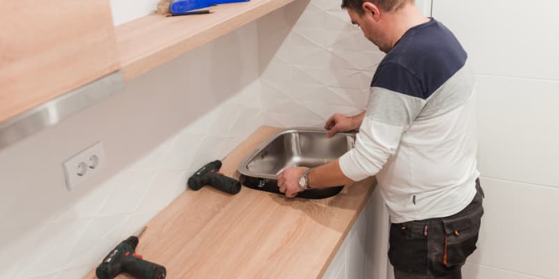 un homme en train de decouper un plan de travail en bois dans une cuisine