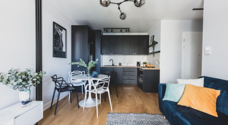 exemple de studio de 30 m2 bien amenage avec canape convertible en velours bleu cuisine noire table a manger ronde laquee blanche petit meuble tv blanc en acier parquet et luminaire boules design