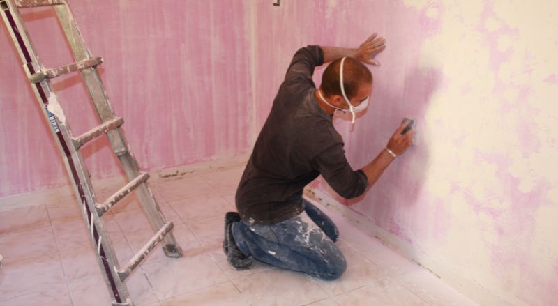 un professionnel equipe d un masque en train de poncer un mur avec une cale a poncer
