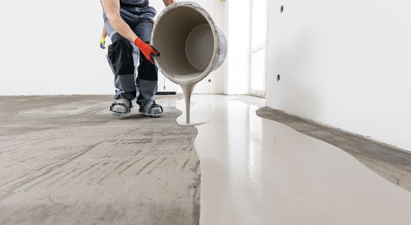 artisan versant une deuxieme couche de mortier de ragreage en interieur