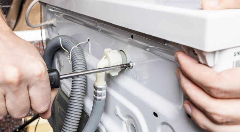 homme demontant un lave linge pour inspecter la pompe de vidange pouvant causer un probleme de refoulement 
