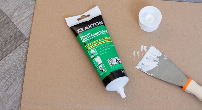 tube d enduit de rebouchage et spatule poses sur un carton