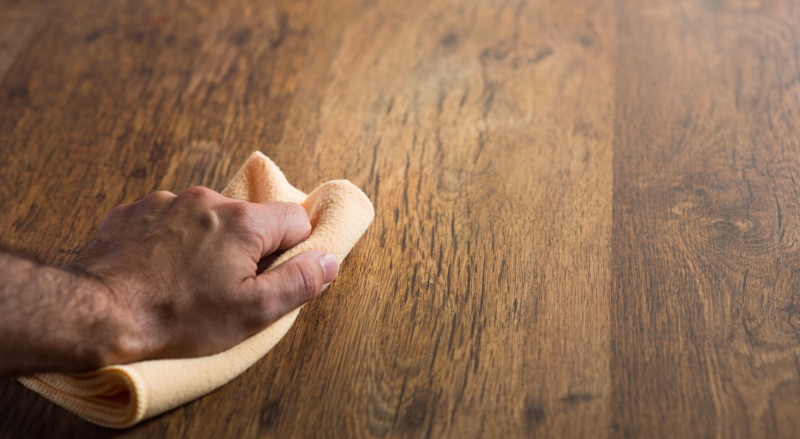 personne qui nettoie de la colle sur un parquet à l'aide d'un chiffon