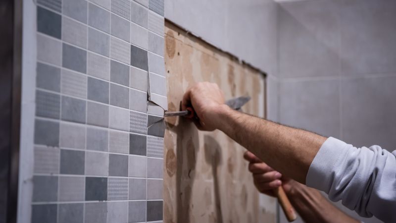 professionnel en train de décoller un carrelage mural dans une salle de bain