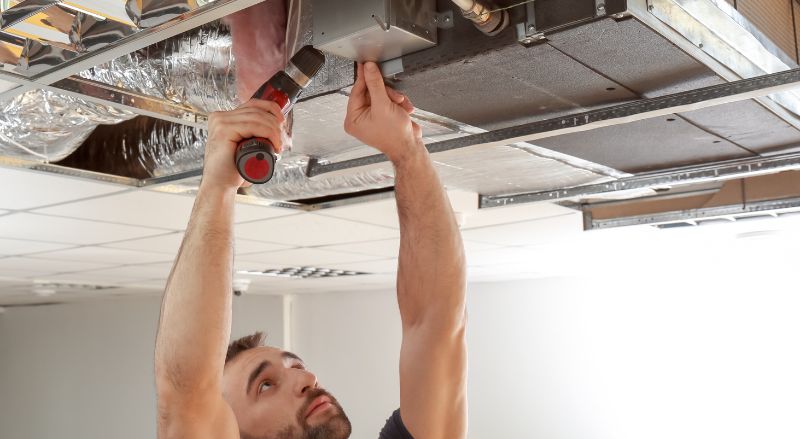 artisan en train de poser moteur vmc et gaines dans un faux plafond