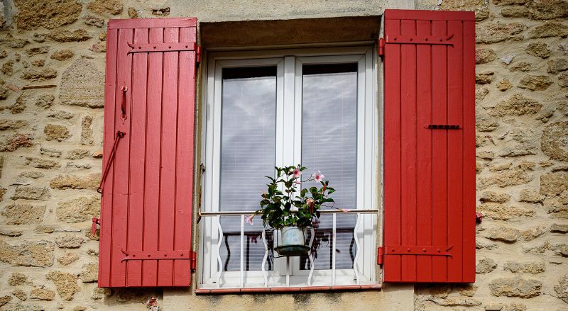 volets rouges sur une maison en pierre